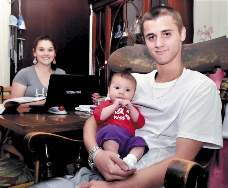 Teenage parents Melinda Pooler, 17, pauses while reading a textbook and working on a computer as Chris Bilodeau, 18, holds their 2-month-old daughter, Abigale, at their home in Waterville on Thursday.
