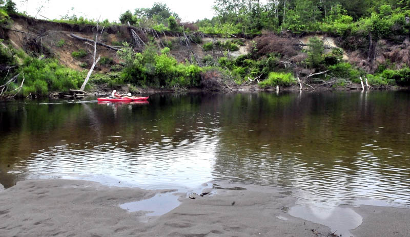 Bill Moloney paddles his kayak past a section of the Sandy River in Farmington, where the banks have eroded near the Whittier Road, top, on Tuesday.