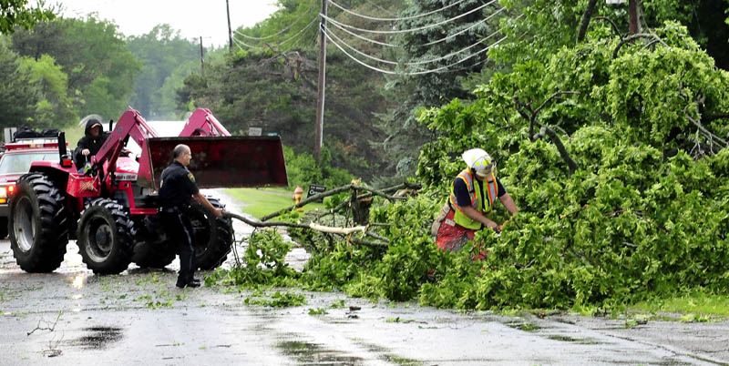 Clinton police officer Stanley Bell, center, pulls limbs away as a Clinton firefighter uses a chainsaw to cut up a tree that fell and blocked a lane on the Hill Road, following a fast-moving storm Tuesday afternoon. At left, neighbor Don Burnham uses his tractor to help.