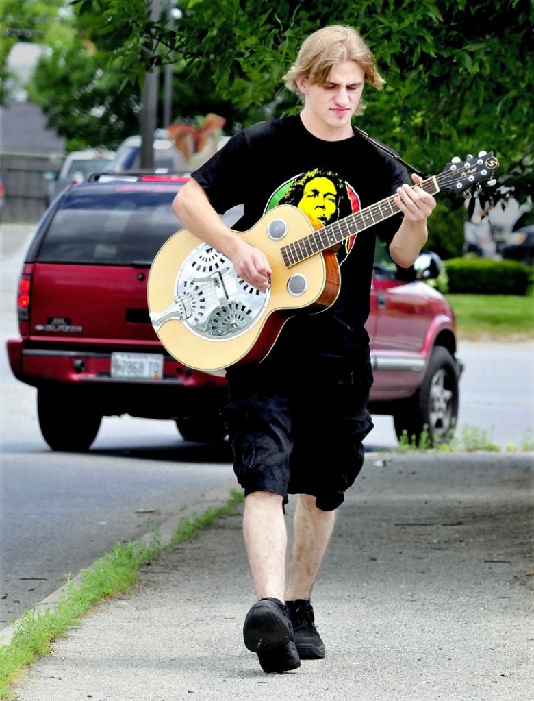 Matt Duest plays his guitar while walking to Walmart in Skowhegan on Monday.