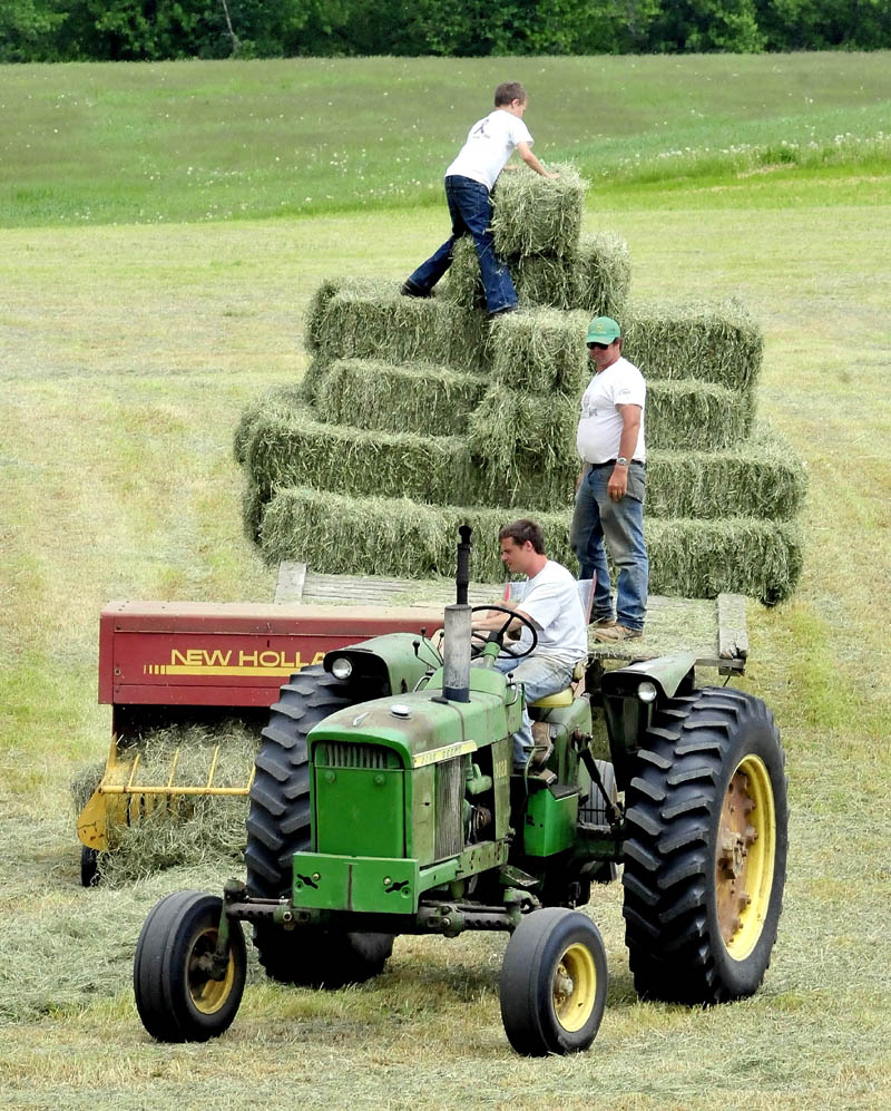 Rick Davis lll operates the tractor as his father Rick Davis ll and son Alex stack hay bales in a field at the Silver Valley farm in New Sharon on Thursday. The farmers were hurrying to beat the next two days of rain.