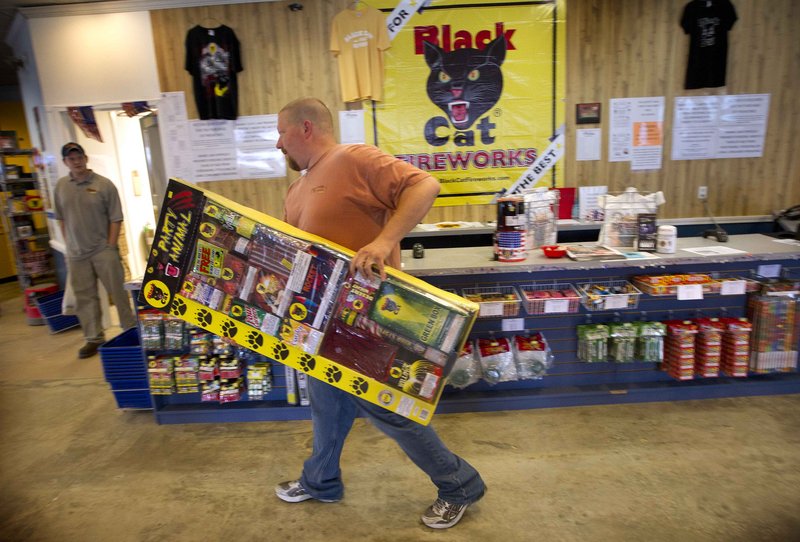 Pyro City Maine worker Zach Gushing carries a jumbo box of aerial and ground fireworks Friday at the Winslow retail store.