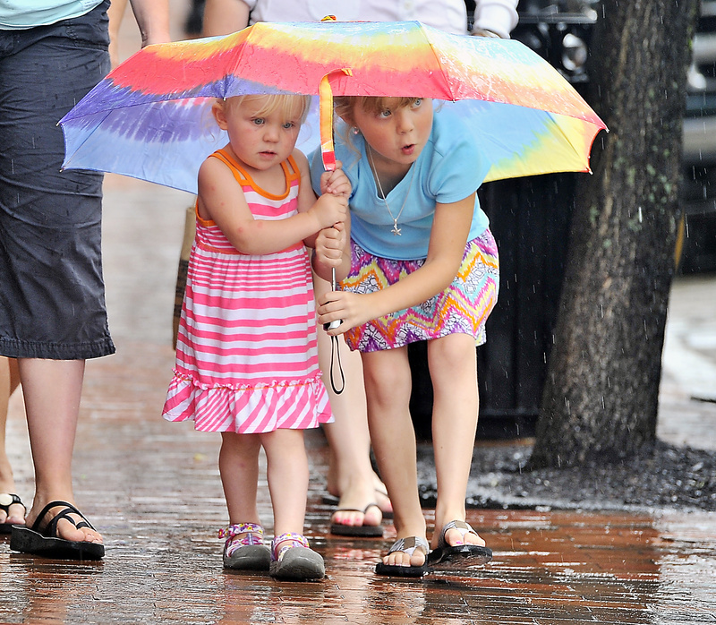Quinn Sawyer, 4, left, and her sister, Summer, 6, take protection from the rain with their colorful umbrella as they walk on Moulton Street in the Old Port with their mother, Jessi Sawyer of Weld, and other family members Monday.