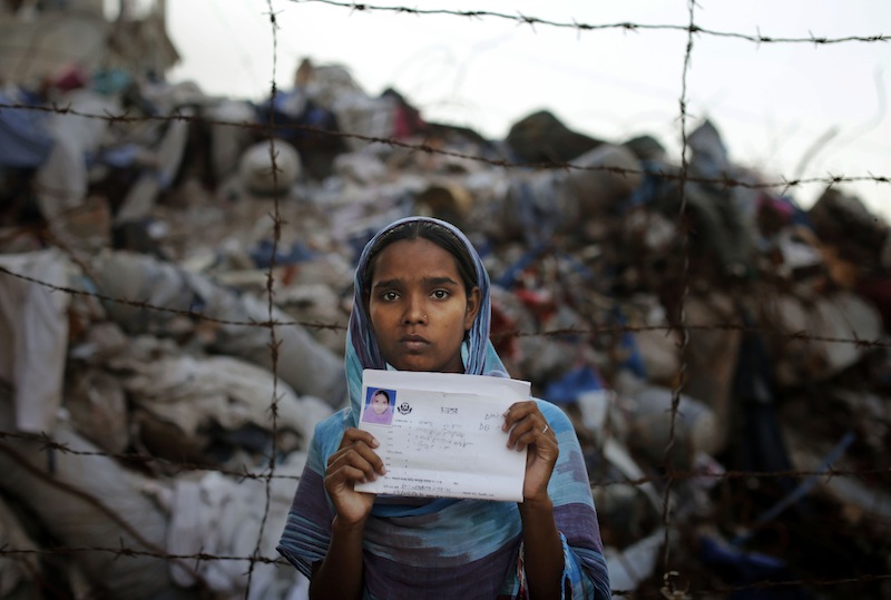 In this June 14, 2013 file photo, Bangladeshi Hashna holds a picture of her sister Josna Khatun, 18 years old, who was a garment worker and is missing following the collapse of the Rana Plaza building poses next to the rubble in Savar, near Dhaka, Bangladesh. A group of 17 U.S. retailers and clothing makers have agreed to a five-year safety pact aimed at improving conditions after the deadliest disaster in the history of the garment industry killed more than 1,100 people. (AP Photo/Kevin Frayer)