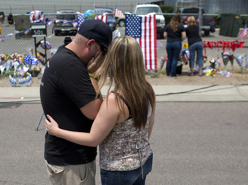 Joanne Barringer, right, comforts her husband Dave Barringer of Las Vegas after hanging a T-shirt on the fence outside the Granite Mountain fire station Monday in Prescott, Ariz. Barringer, who said he works as a firefighter for the U.S. Forest Service, said he was friends with many of the 19 Hotshots who were killed Sunday when an out-of-control blaze overtook the elite group near Yarnell, Ariz.