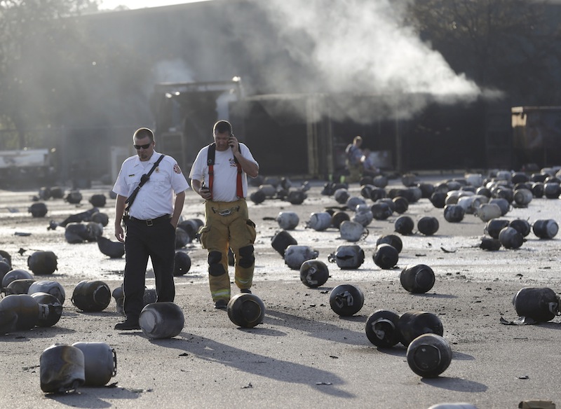 Firefighters walk through an area of exploded propane cylinders in the aftermath of an explosion and fire at a propane gas company, Tuesday, July 30, 2013, in Tavares, Fla. Eight people were injured, with at least three in critical condition. John Herrell of the Lake County Sheriff's Office said early Tuesday there were no fatalities despite massive blasts that ripped through the Blue Rhino propane plant late Monday night. (AP Photo/John Raoux)