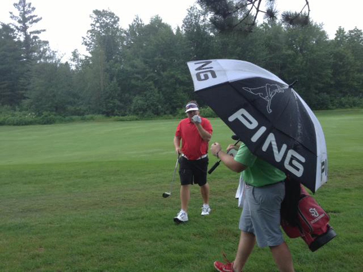 Ryan Gay, left, heads for shelter under an umbrella while playing the sixth hole during a downpour today at the Maine Amateur at the Augusta Country Club in Manchester. Play was suspended at 11:55 a.m. and then resumed around 1:00 p.m. as weather cleared.