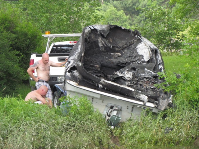 Two unidentified men trailer a boat that burned on the Kennebec River, in Pittston on Friday.