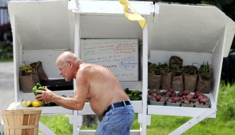 Roy Harrington stacks cucumbers that he dipped in water at the farm stand next to his family's plot in Manchester on Sunday. Harrington said he's transitioning from a semi-retired small engine mechanic to a full-time farmer, with his vegetable garden and selection of fruits.