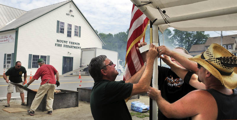 Mount Vernon firefighters John Dearborn, right, Doug Stevens and Dana Dunn hang an American flag Sunday while other volunteers flip racks of chicken barbecuing in scorching heat for the department's annual chicken barbecue in the center of the village. Members of the volunteer company prepare and sell between 500 and 600 meals every year to raise money for the department, Chief Dana Dunn said. This year marks the 40th anniversary of the community cookout, according to Dunn.