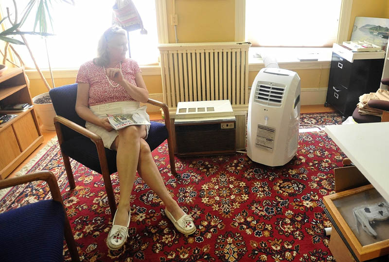 Jennifer Kierstead sits next to her brand new energy efficient air conditioner that is replacing the older air conditioner in her downtown Waterville office on Tuesday. As temperatures rise, Central Maine Power is asking customers to limit their power usage.
