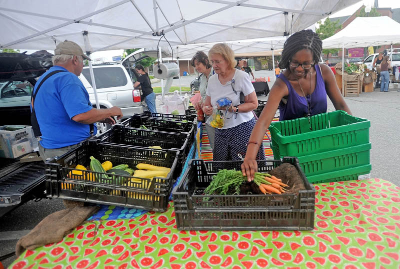 Noma Moyo, 21, a Colby College junior, picks up fresh carrots from 100 Acre Farm, at the Waterville Farmers' Market at the Concourse on Thursday.