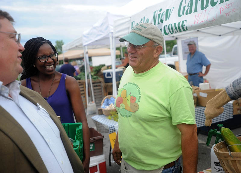 Fred Nassar, right, with Eagleview Gardens and Haunted Trail Pumpkins in Winslow, offers produce to Colby College student Noma Moyo, 21, background, and Joe Klaus, left, at the Waterville Farmer's Market at the Concourse on Thursday.