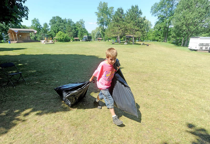 Hunter Desveaux, 12, hauls bags of trash to a waiting truck as he helps clean up after the Winslow Family 4th of July Celebration at Fort Halifax Park in Winslow on Friday.