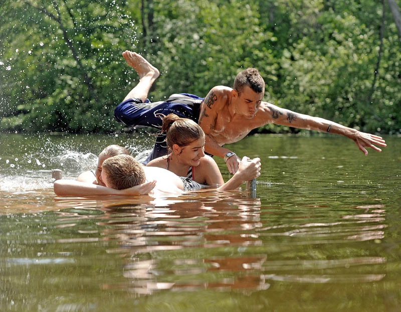Travis Decato, 20, leaps over his friends, Jennifer Stanphill, 19, right, Joe Andrews, laying on the deck, bottom center, and Samantha Thomas, 21, hidden, in to the Messalonskee Stream in Waterville on Saturday.