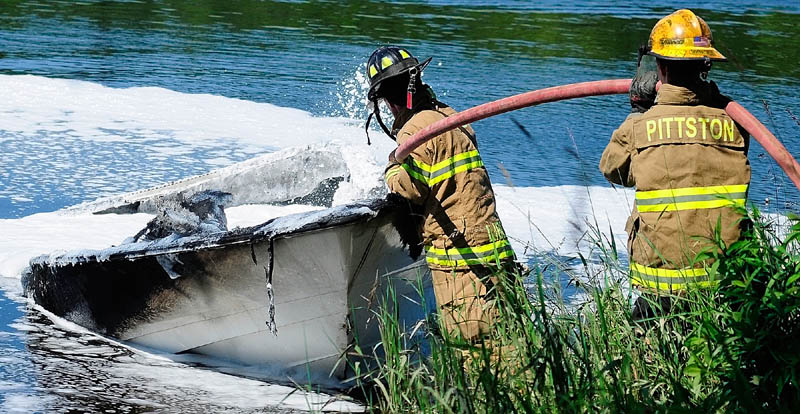 Firefighters on shore spray foam on a burned boat on Friday on the banks of the Kennebec River, near Togus Stream in Pittston.