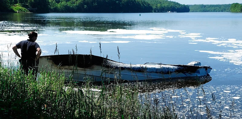 State Fire Marshal's Office Investigator Mary MacMaster looks over a burned-out boat on Friday on the banks of the Kennebec River, near Togus Stream in Pittston.