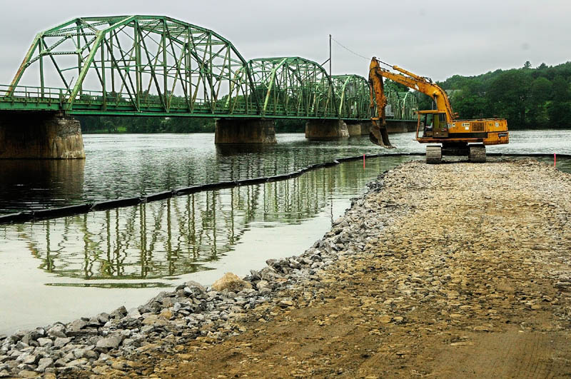 An excavator spreads a load of stone Wednesday as Reed & Reed Construction workers build a construction causeway for the work on the bridge over the Kennebec River to Richmond.