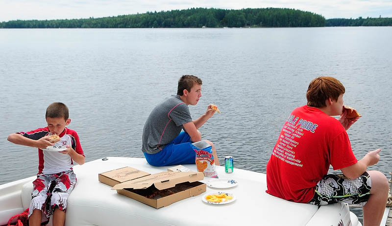 Cousins Daniel McCray, 9 of Augusta, Jordan Martel, 15 of Palm Bay, Fla., and Trevor McCray, 14, of Sidney, eat pizza on the back of a boat docked behind Day's Store on Thursday in Belgrade Lakes. They were taking a break from tubing on Long Pond with their grandfather.