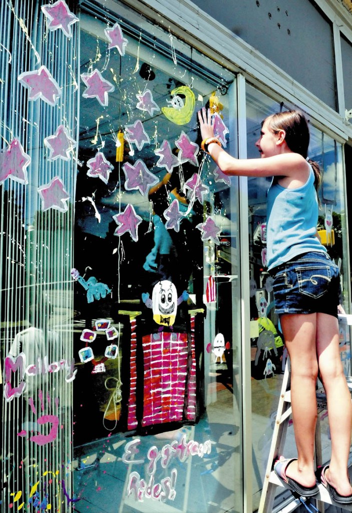 Mallory Whitney reaches up to place a hand print, while taking part in window painting on Main Street in Pittsfield on Thursday. The event was part of the week-long Central Maine Egg Festival.