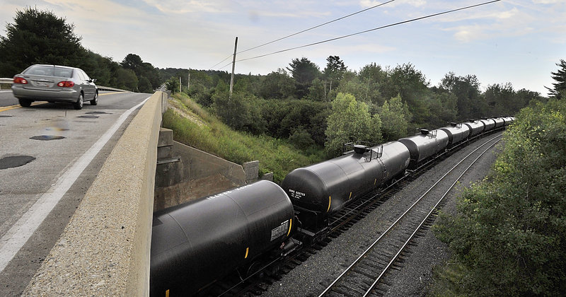 A car passes over the bridge near a line of Petroleum Crude Oil transport rail cars as they sit near Route 115 in Yarmouth on Tuesday, July 23, 2013.