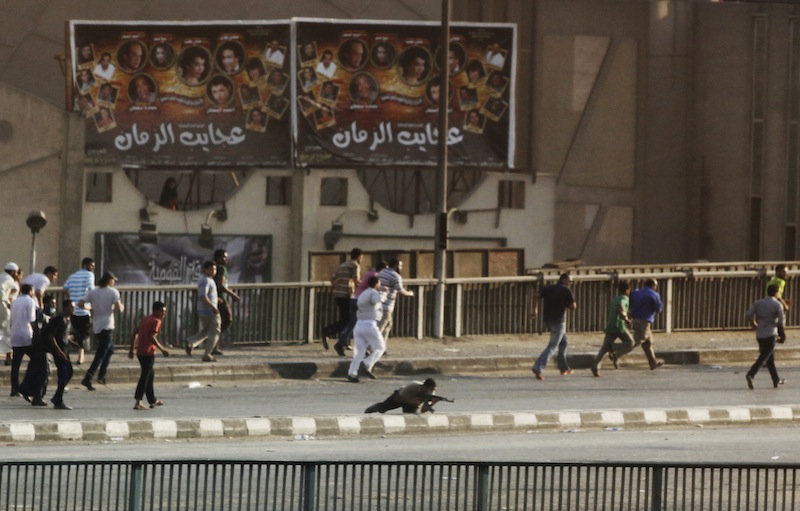A man, center, holding a gun takes his position while having gunfire with other civilians in Cairo, Egypt, Friday, Aug. 16, 2013. Gunfire rang out over a main Cairo overpass and police fired tear gas as clashes broke out after tens of thousands of Muslim Brotherhood supporters took to the streets Friday across Egypt in defiance of a military-imposed state of emergency following the country's bloodshed earlier this week. (AP Photo/Manoocher Deghati)