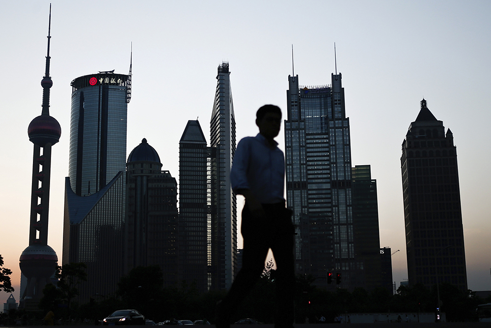 In this photo taken July 10, 2013, a man walks past the downtown skyline of Shanghai, China. China’s consumer inflation held steady in July and a fall in producer prices decelerated in a new sign a slump in the world’s second-largest economy might be stabilizing. (AP Photo)