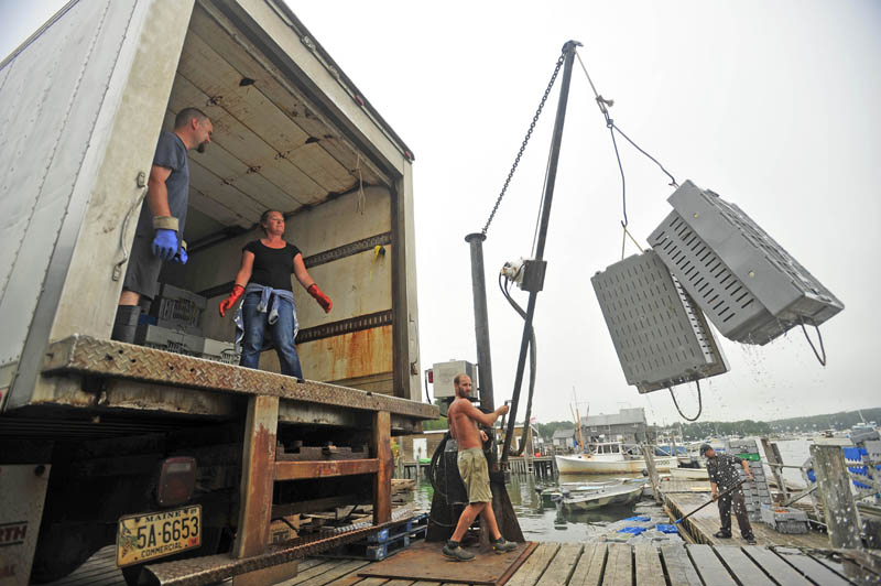 Heidi Simmons, center, stands inside the transport truck as Craig Mott, 36, right, dock manager at the Friendship Lobster Co-op in Friendship Harbor, helps load crated lobsters onto a truck bound for a sorting facility in the town of Bremen on July 29.