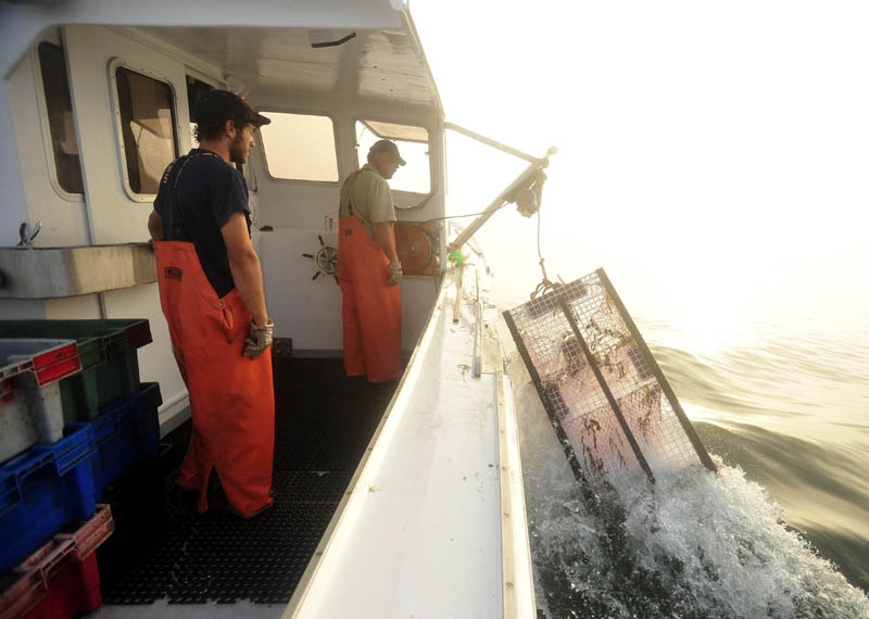 Jim Wotton, 44, center, hauls in a lobster trap with his nephew and deckhand, Carl Hayse, 18, left, while fishing between Allen's Island and Mosquito Rock on July 24.