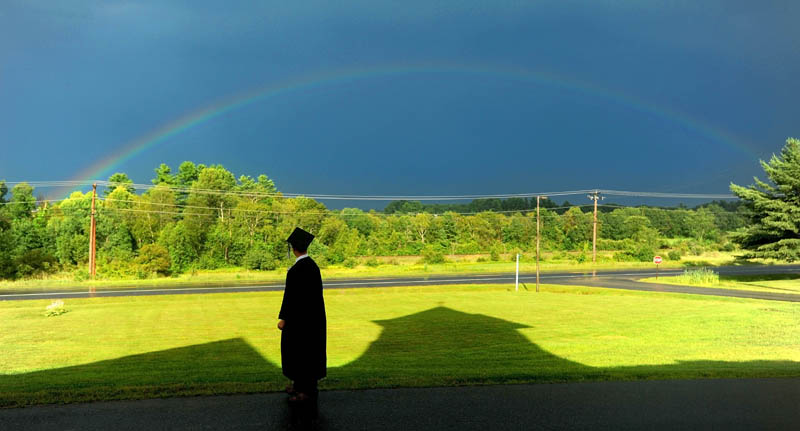 Cody Buzzell, 17, stands in the shadow of Moody Chapel as a rainbow shines over Hinckley, before the Maine Academy of Natural Sciences' inaugural commencement today.