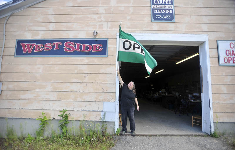 Sue LeJoy hangs an "Open" flag at the front door of the West Side store and Cole's Carpet and Upholstery Cleaning Service, at 33 Madison Ave. in downtown Madison, today.