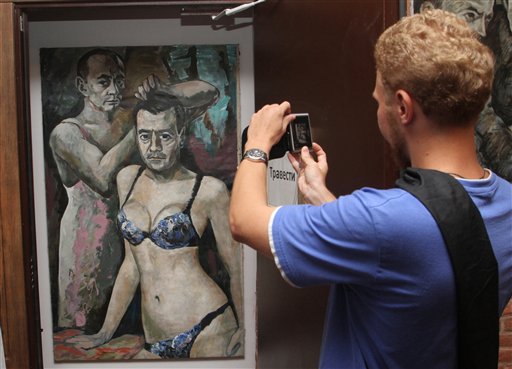In this photo Aug. 15, 2013, photo, a visitor photographs the artwork entitled "Travesty" by Konstantin Altunin at an exhibition in St. Petersburg, Russia. Four controversial paintings satirizing Russian politicians were removed from the exhibition on Tuesday.