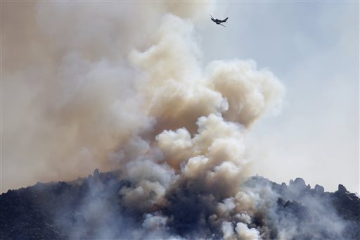 A small plane flies over a wildfire burning near Banning, Calif., on Thursday. About 1,500 people have fled and three have been injured as a wildfire in the Southern California mountains quickly spreads. Several small communities have evacuated.