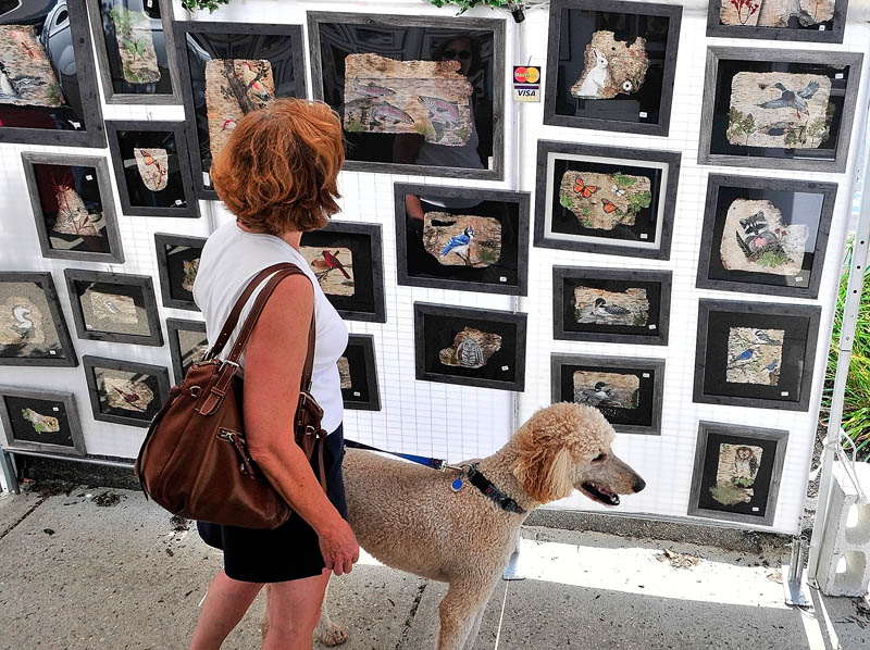 Debbie Farrell and her poodle, Rigby, look at Sharon Boody-Dean's paintings on birch bark during the 26th annual Winthrop Sidewalk Art Show today in downtown Winthrop.