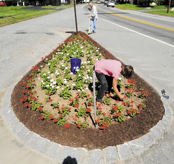 Bill Meyer, top, and Winter Webb clean up and weed a traffic island on Friday in Belgrade Lakes. Meyer said they had been weeding and sweeping around the island every Friday this summer.
