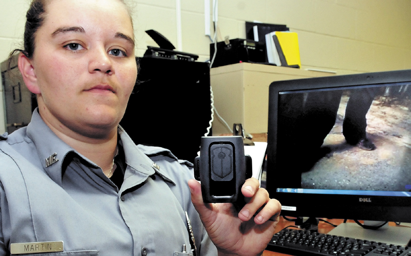 Wilton police officer Billie Martin holds a small Cop Vu camera that can be worn on an officer's uniform. A visual and audio recording of a recent incident, recorded by the camera, is displayed on a nearby computer screen.