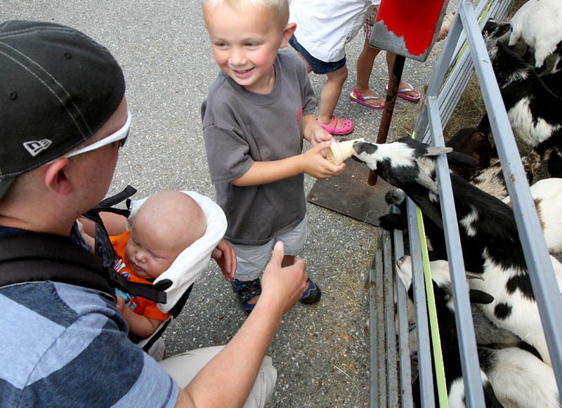 A miniature goat grabs a snack cone from three-year-old Jackson Munger of Pittsfield while at the the Taste of Greater Waterville on Wednesday. With Jackson is his dad Andrew and four-month-old brother Brantley.