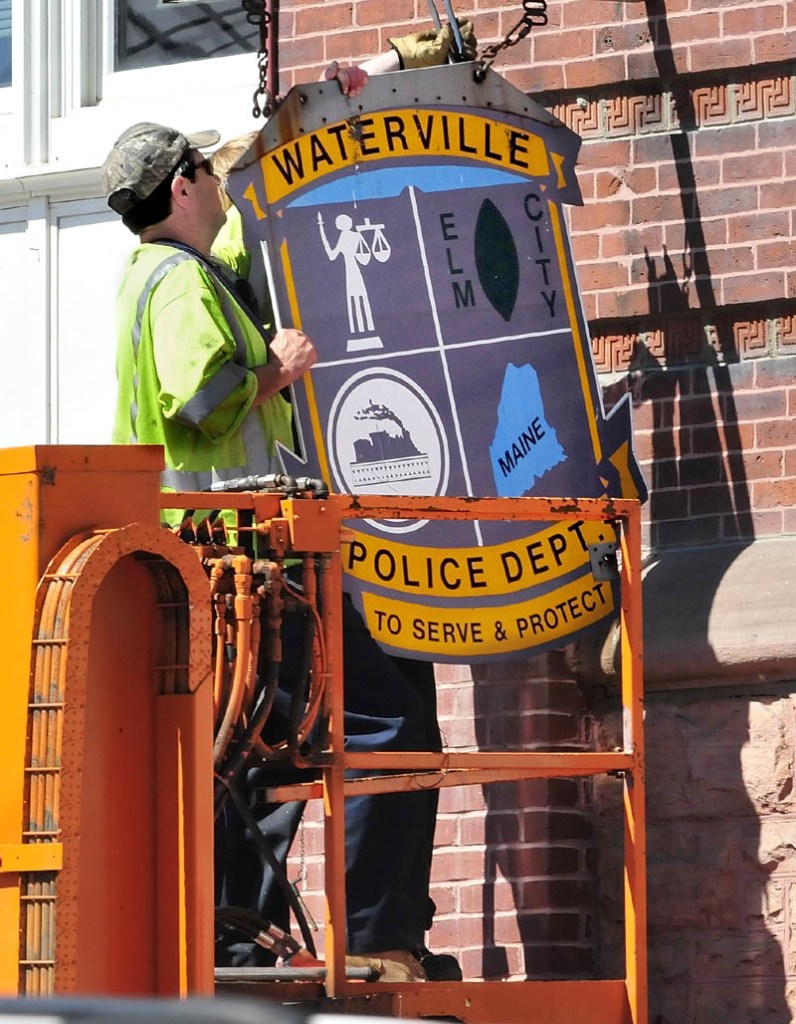 David Main, left, and Jacob Chambers of the Waterville public works department remove the Waterville Police Department sign on City Hall on Aug. 1. City councilors on Tuesday will consider spending $85,000 to renovate the former headquarters of the department, to allow for expansion of other departments to the space.