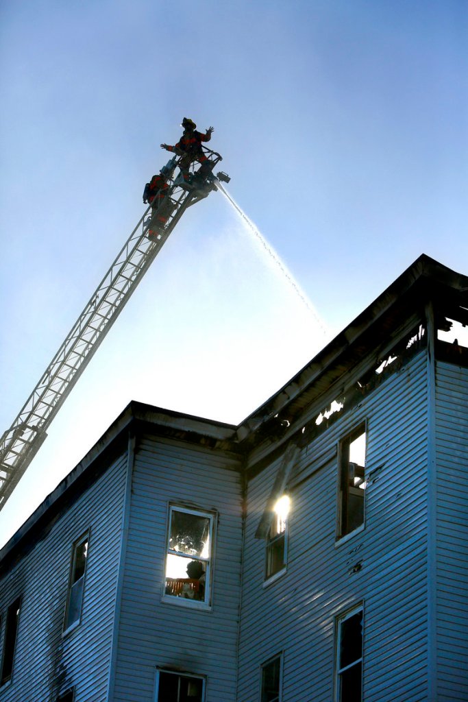 Maine Sunday Telegram file photo/Tim Greenway Firefighters spray water on the roof of a vacant apartment building on Bartlett Street in Lewiston on May 6. The building was razed after being destroyed by the arson fire.