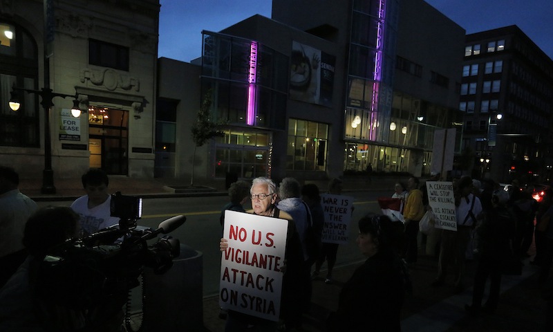 Wells Staley-Mays of Portland, who has visited Syria, holds a sign while conducting a television interview during a gathering in Monument Square on Monday evening, Sept. 9, 2013, to protest proposed military action in Syria by the United States.