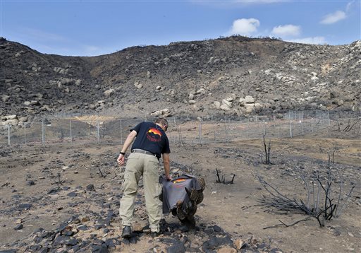 Prescott Wildland Division Chief Darrell Willis touches a Granite Mountain Hot Shots crew shirt draped over a burned cactus, in Yarnell, Ariz., on July 23. A three-month investigation into the June deaths of 19 firefighters killed while battling an Arizona blaze cites poor communication between the men and support staff, and reveals that an airtanker carrying flame retardant was hovering overhead as the men died.