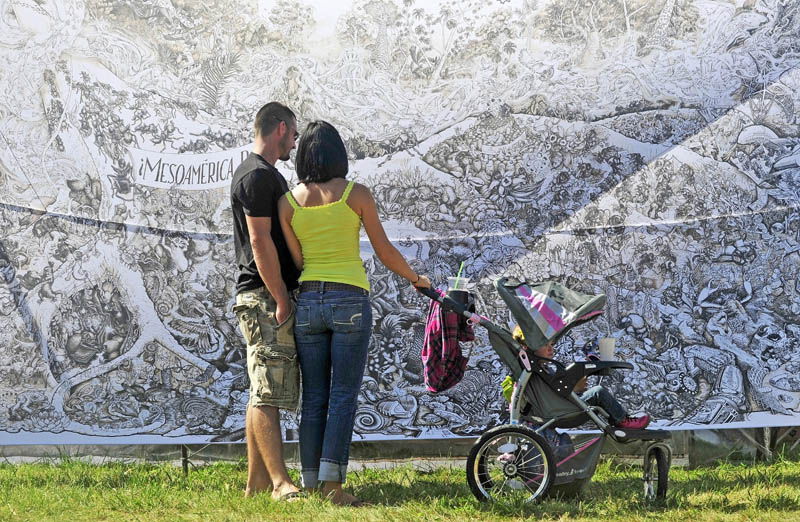 Nate Sprague, left, and Madeleine Hill, center, with her 2-year-old daughter, London Wallace, view the MesoAmerica drawing by the Beehive Design Collective on display at the Common Ground County Fair in Unity today.