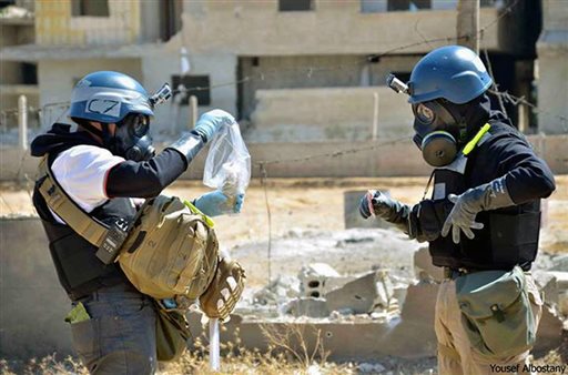 In this Aug. 28, 2013, image provided by the United Media Office of Arbeen, members of the UN investigation team take samples from sand near a part of a missile that is likely to be one of the chemical rockets according to activists, in the Damascus countryside of Ain Terma, Syria.