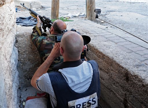 In this Wednesday, Sept. 11, 2013, photo released by the Syrian official news agency SANA, a journalist records a Syrian government soldier as he aims his weapon, during clashes with Free Syrian Army fighters in Maaloula village, northeast of Damascus, Syria.