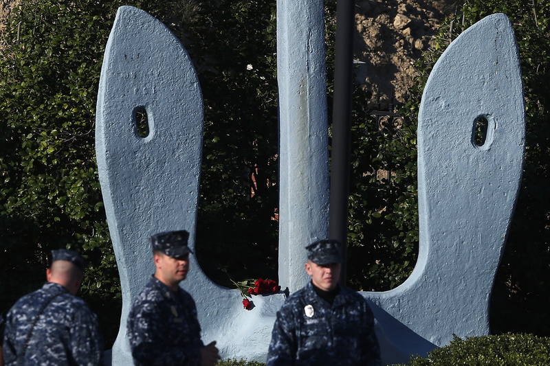 Roses that were placed on an anchor at an entrance of the Washington Navy Yard are seen behind security personnel as they stand watch Thursday. The Washington Navy Yard began returning to nearly normal operations three days after it was the scene of a mass shooting in which a gunman killed 12 people.