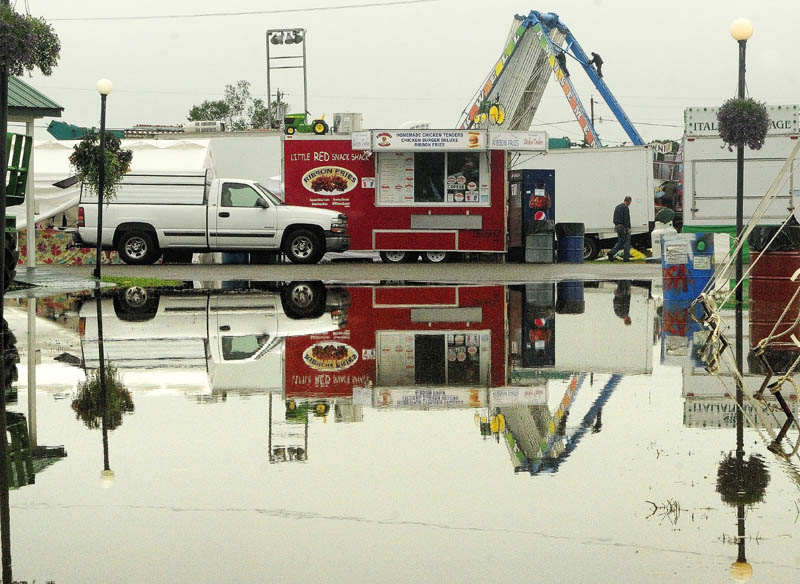 Workers climbing down from dismantling the Ferris wheel are reflected in a large puddle today at the Windsor Fair. Except for the 4-H livestock auction, all fair events were cancelled today because of the heavy rain in the morning.