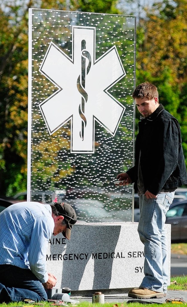 Robert Antognoni, left, hooks up wires for LED lights as Robert E. Antognoni waits with a remote control to test them on Thursday at the Maine Emergency Medical Services monument being built in in Augusta. The father and son electricians, from Randolph, were wiring up the lights that will shine from under the clear monument on State Street, between the police and fire memorials on the State House complex grounds.