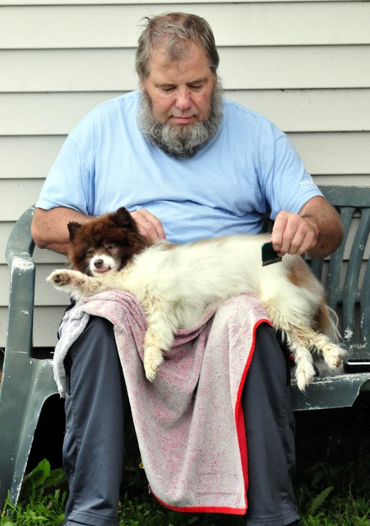 Coco the dog relaxes in the lap of Cecil Parsons as he combs the dog's hair in Waterville recently.