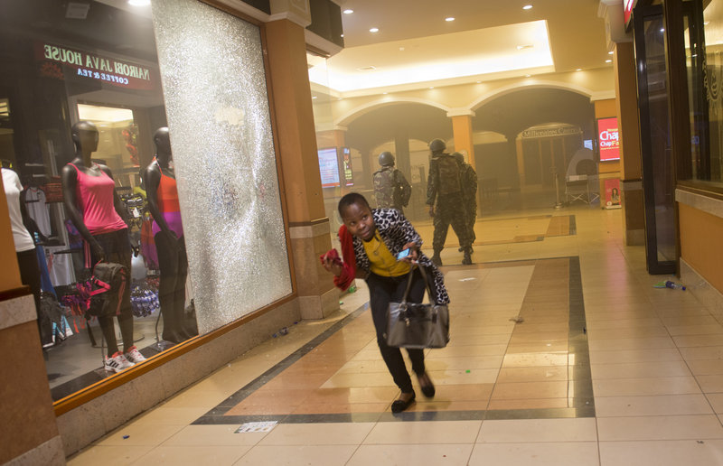 A woman who had been hiding during the gun battle runs for cover after armed police, seen behind her, enter the Westgate Mall in Nairobi, Kenya, on Saturday.