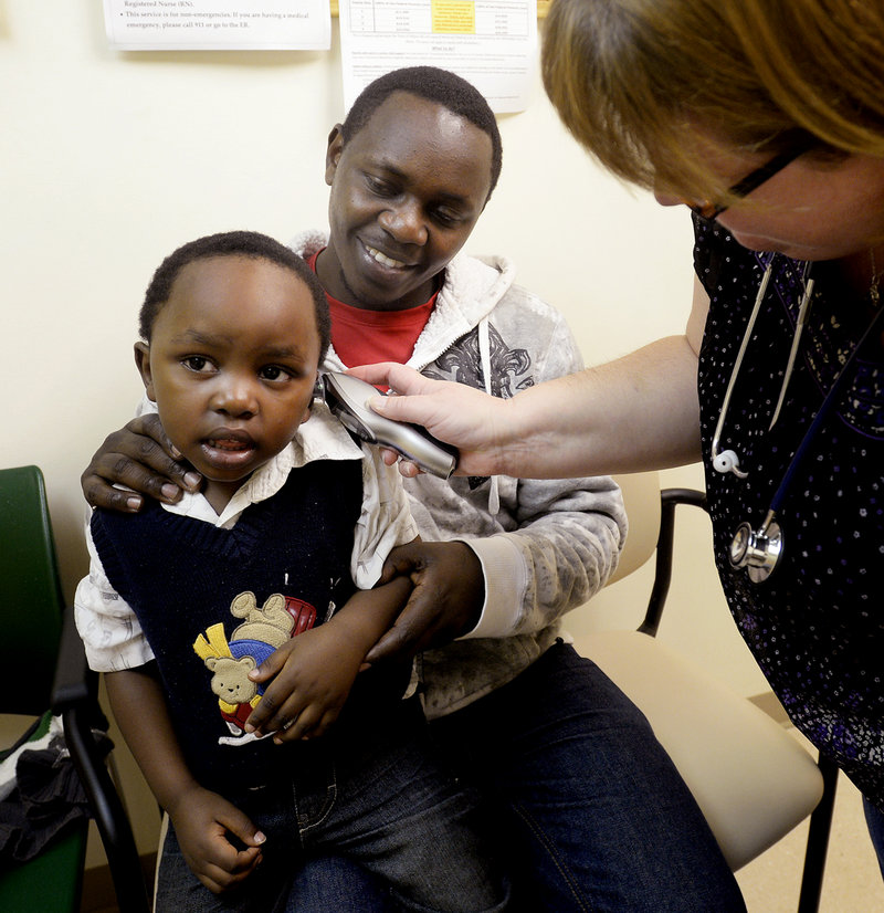 Miraji Imena, 2, is held by his father, Joseph Nsabimana, as he has his temperature taken by medical assistant Susan Huff at the Portland Community Heath Center on Friday.